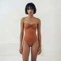 Woman wearing a rust-colored strapless swimsuit against a white background