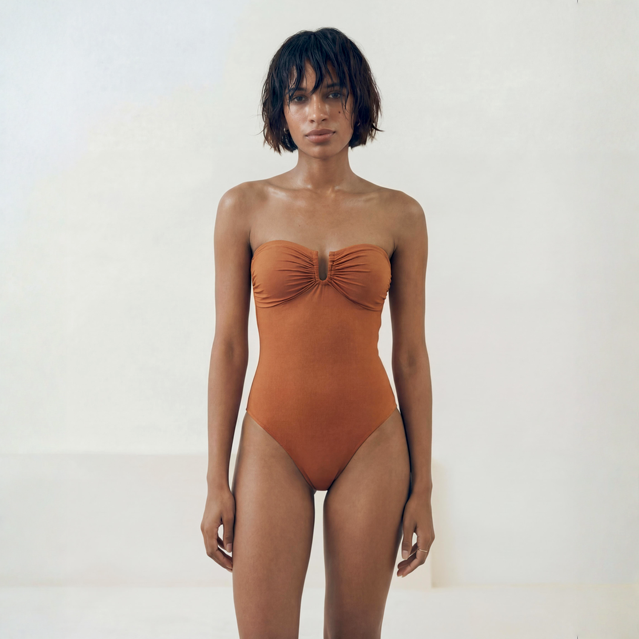 Woman wearing a rust-colored strapless swimsuit against a white background