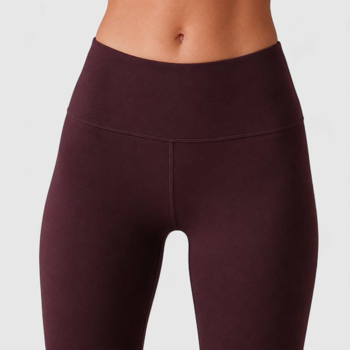 Close-up of a model wearing high-waisted leggings in a deep plum or eggplant shade against a light gray studio background.